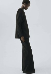 Black tailored suit featuring a long blazer and flared trousers, made from smooth fabric with clean lines and minimal detailing.