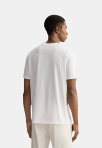 T-shirt bianco in cotone con maniche corte, scollo rotondo e vestibilità rilassata. Il tessuto appare liscio con dettagli di cucitura minimi.