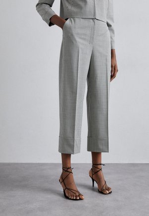 Pantaloni cropped in bianco e nero a motivo houndstooth con tasche laterali, caratterizzati da una vestibilità su misura e orli arrotolati, abbinati a tacchi neri con cinturini.