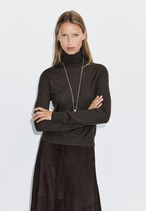 Brown turtleneck sweater made of soft fabric, fitted design with long sleeves, paired with a dark brown skirt. Minimalist silver necklace.