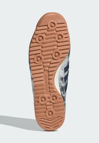 Semelle de chaussure de sport avec une finition en caoutchouc texturé. Présente des motifs de grip circulaires et un design plat et large avec une couleur brunâtre-orange.