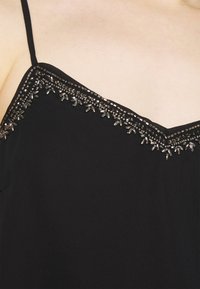 Camiseta sin mangas negra con escote en forma de V, adornada con detalles de cuentas plateadas y lentejuelas transparentes a lo largo del borde.