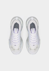 Ζευγάρι λευκά παπούτσια τρεξίματος Under Armour με κορδόνια, διχτυωτές επιφάνειες και γλώσσες με το λογότυπο, εμφανίζεται σε μία λήψη από πάνω με απλό φόντο.