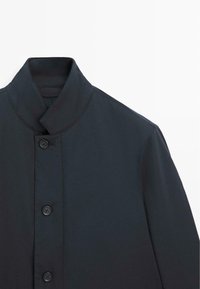 Mørkegrå jakke med høj krave, der har en glat tekstur, fem knapper og et rent, minimalistisk design uden yderligere mønstre.