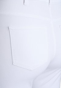 Pantalones de mezclilla blancos con vista trasera que presenta un solo bolsillo trasero y detalles de costura visibles, mostrando un acabado suave y texturizado.