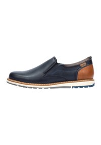 Zapato náutico de cuero azul marino, con acentos de cuero marrón, suela blanca, costuras en contraste y punta redondeada. Presenta paneles laterales elásticos para un mejor ajuste.