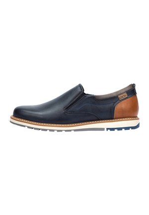 Zapato náutico de cuero azul marino, con acentos de cuero marrón, suela blanca, costuras en contraste y punta redondeada. Presenta paneles laterales elásticos para un mejor ajuste.