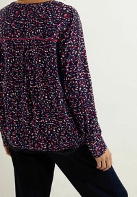 Blouse à manches longues en marine avec un imprimé coloré et abstrait. Présente un col rond et un dos froncé pour plus de texture et de détail.