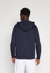 Sweatshirt à capuche bleu marine avec une poche kangourou, des poignets et un ourlet côtelés. Fabriqué en tissu doux, il présente une coupe décontractée et un design simple.