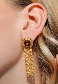 Des boucles d'oreilles en or avec une pierre carrée en ambre entourée d'un design de cordon torsadé, avec une frange en chaîne dorée qui descend en dessous.