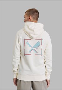 Cremefarbener Hoodie mit einem lebendigen Motiv von gekreuzten Messern, eingerahmt von blauen und roten Strichen auf der Rückseite. Baumwollmaterial, lässige Passform.