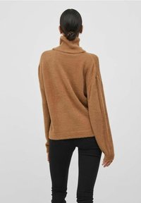 Hnědý, načechraný rolák s dlouhými, oversized rukávy. Tkanina vypadá měkce a teple, s volným střihem a minimalistickým designem.