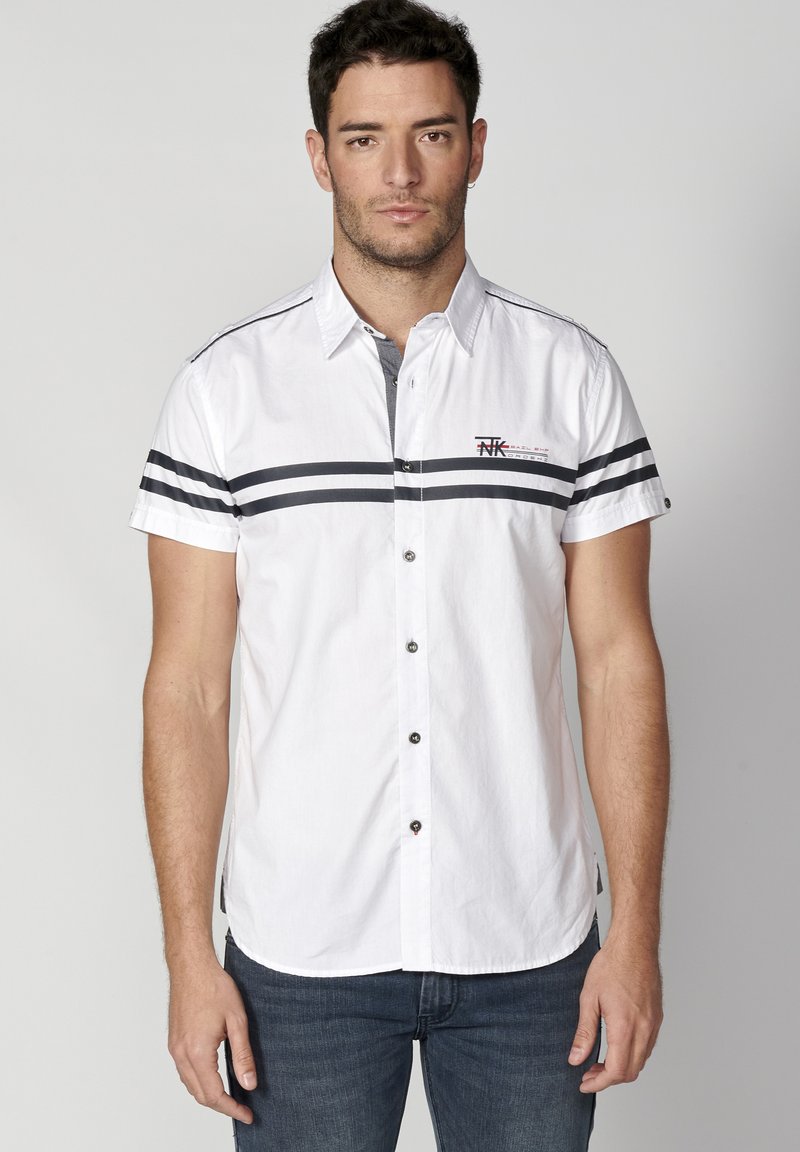 Camisa blanca de manga corta con rayas horizontales negras y un pequeño logo. Diseño con botón y dobladillo redondeado, y cuello en contraste gris.