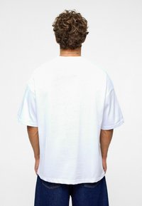 Witte oversized T-shirt van katoen, met verlaagde schouders en een rechte zoom. De achterkant toont een gladde textuur en geen ontwerpdetails.