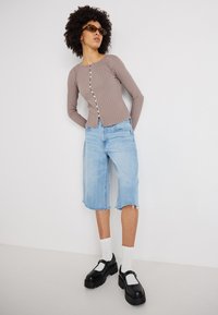 Top cu maneci lungi ribbate de culoare maro deschis, cu deschidere cu butoane, combinat cu șorturi din denim de lungime până la genunchi de culoare albastru deschis. Pantofi cu platformă negri și șosete albe.