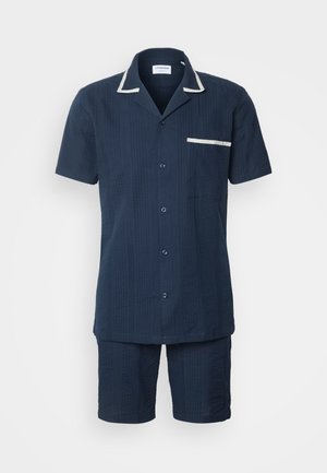 Marineblå kortærmet skjorte og matchende shorts sæt, struktureret stof med et subtilt stribet mønster. Hvid kant ved krave og brystlomme.