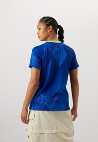 Short-sleeve athletic shirt in vibrant blue with geometric patterns. Features a rounded neck with a lime green accent and a lightweight texture.