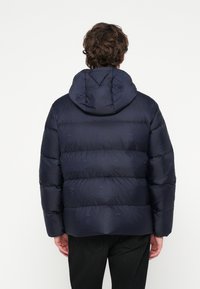 Navyblaue Steppjacke mit Kapuze, Knopfdetails und einem dezenten, geprägten Muster, mit gesteppter Konstruktion für Wärmeisolierung.