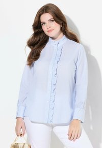 Světle modrá pruhovaná košile s knoflíčky, volánkovým límcem a dlouhými rukávy. Bílé knoflíky a manžety zvýrazňují design. Hladká textura látky.