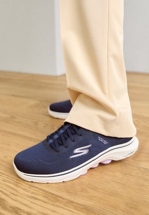 Zapatillas deportivas azul marino con parte superior de malla, puntera redonda y suela blanca. Presenta un logo en el costado y detalles en rosa en la suela.