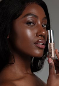 Glasmarker-Tube mit silberner Kappe und klarem Körper, nahe dem Gesicht eines Modells gehalten, das ihre glatte, strahlende Haut zeigt.