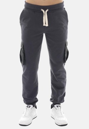 Pantalon jogger cargo bleu marine avec taille à cordon et poches latérales, porté avec des baskets blanches sur un fond uni.