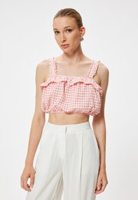 Top crop de cuadros vichy en rosa y blanco con hombros con volantes y un corte holgado, combinado con pantalones de tiro alto en blanco. Textura de tela suave.