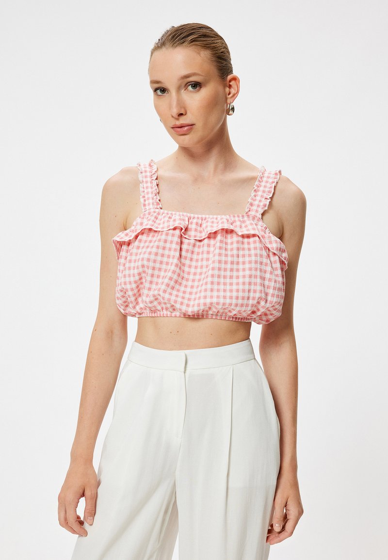 Top crop de cuadros vichy en rosa y blanco con hombros con volantes y un corte holgado, combinado con pantalones de tiro alto en blanco. Textura de tela suave.