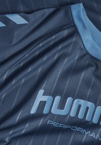 Blaues Sportshirt mit hellblauem Kragen und aufgedrucktem "hummel PERFORMANCE"-Logo, mit dezenten vertikalen Nadelstreifen und Chevron-Design auf der Schulter.
