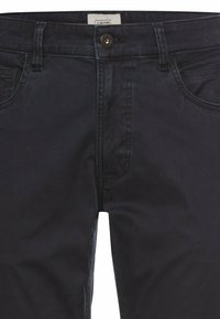 Dark navy jeans with a straight leg design, front pockets, a button closure, and subtle texture. White label visible on the back waistband.