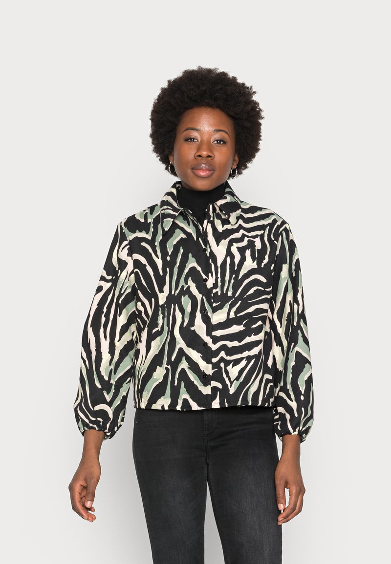 Casaco cropped em padrão zebra preto, verde e branco; apresenta colarinho de camisa e fechamento com botão; mangas longas e bufantes.