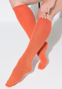 Calze arancioni fino al ginocchio con una texture a coste, caratterizzate da una finitura liscia e una vestibilità elasticizzata. Nessun motivo o dettaglio visibile.