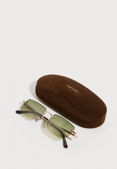 Ορθογώνια γυαλιά ηλίου με πράσινη απόχρωση και χρυσό πλαίσιο δίπλα σε καφέ βελούδινη θήκη με ανάγλυφη τη λέξη "TOM FORD" σε χρυσά γράμματα.