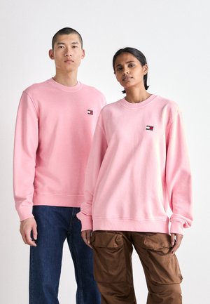 Sudaderas rosas con cuello redondo y hombros caídos, que presentan un pequeño logo en contraste en el pecho. Modeladas por dos personas.
