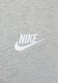 Harmaa puuvillakankaita, jossa on valkoinen brodeerattu Nike-logo, esittelee sileää tekstuuria ja rentoa muotoilua.