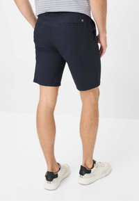 Pantaloni corti blu navy realizzati in un tessuto leggero, dotati di tasche laterali e posteriori. Il design presenta una texture liscia e orli risvoltati.