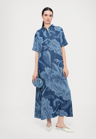 Rochie din denim de culoare albastră închisă, cu un model floral mare, mâneci scurte, guler și fante laterale. Asortată cu o geantă albastră și espadrile albe.