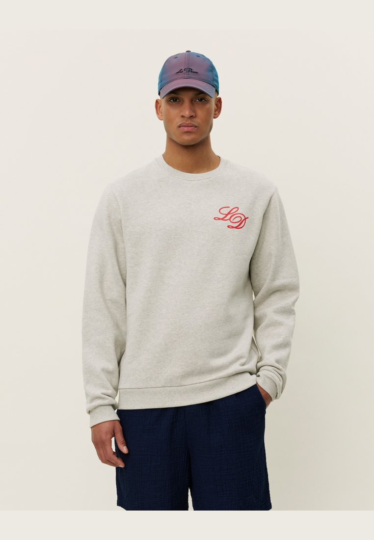 Light grey sweatshirt with ribbed cuffs and hem, featuring a red "LD" logo on the chest. Worn with navy blue shorts and a multicolored cap.