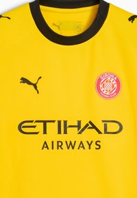 Żółta koszulka piłkarska z krótkim rękawem, z czarnym okrągłym dekoltem, czarnym logo Pumy, napisem ETIHAD AIRWAYS oraz okrągłym herbem Girona FC.
