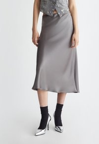 Gonna midi in satin grigio con una texture liscia, leggermente svasata e un orlo che cade. Abbinata a calze arricciate nere e tacchi argentati.