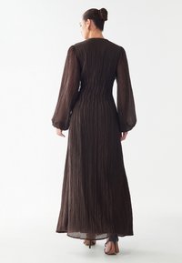 Rjava plisirana maksi obleka z dolgimi rokavi, ki ima tesno prilegajoč bodič in tekočo krilo. Prosojna tkanina z teksturnim zaključkom.