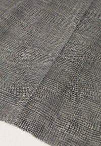 Tissu à carreaux gris et noir avec une texture tissée, couches superposées montrant un motif et une structure détaillés.