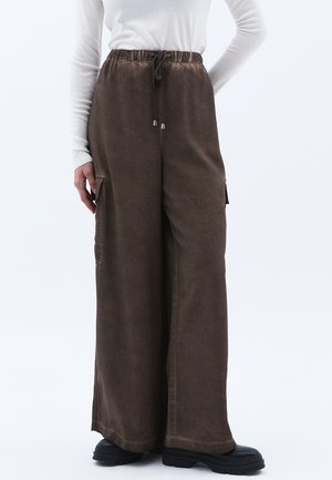 Braune weit geschnittene Cargo-Hosen mit einem elastischen Taillenbund mit Kordelzug, seitlichen Taschen und einer glatten Stofftextur, kombiniert mit schwarzen Knöchelschuhen.