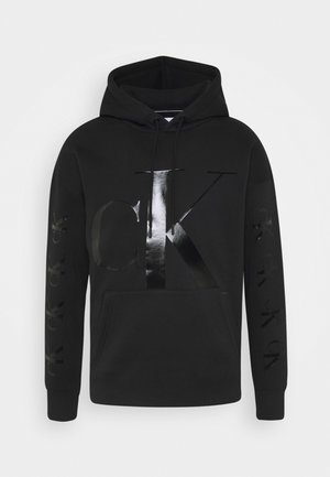 Czarna bluza z kapturem z dużym błyszczącym logo "CK" z przodu oraz powtarzającymi się tłoczonymi logo "ck" na obu rękawach, kieszeń z przodu.