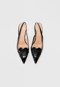 Melna patentā ādas slingback zābaki ar norādītām purngalēm, sirds formas detaļām un loku akcentiem. Zelta logo uz iekšpuses. Gluda tekstūra.