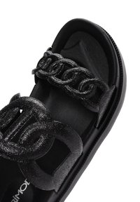 Sandalias negras con una suela de goma texturizada negra y dos correas con un patrón de cadena brillante para el cierre.