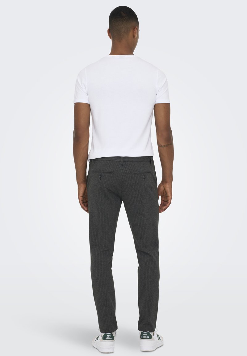 Pantaloni a righe grigie con taglio slim, abbinati a una maglietta bianca semplice e sneakers bianche con dettagli verdi e logo.