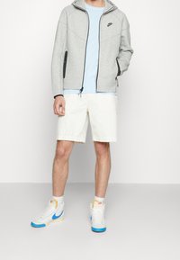 Harmaa vetoketjullinen huppari mustilla yksityiskohdilla, vaaleansininen t-paita, valkoiset cargoshortsit ja korkeat tennarit, joissa sinisiä ja keltaisia yksityiskohtia.