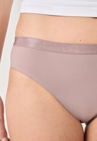 Jasnoróżowe bikini z gładką fakturą, z błyszczącemu, różowozłotemu paskowi. Projekt jest minimalistyczny i dopasowany.