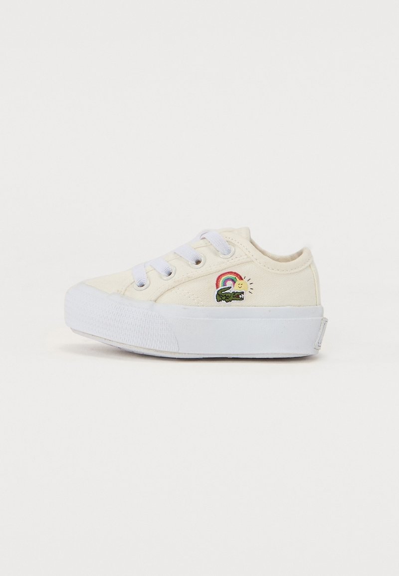 Baskets en toile blanche avec une semelle texturée, comportant trois œillets blancs et un motif brodé d'un arc-en-ciel et du soleil sur le côté.
